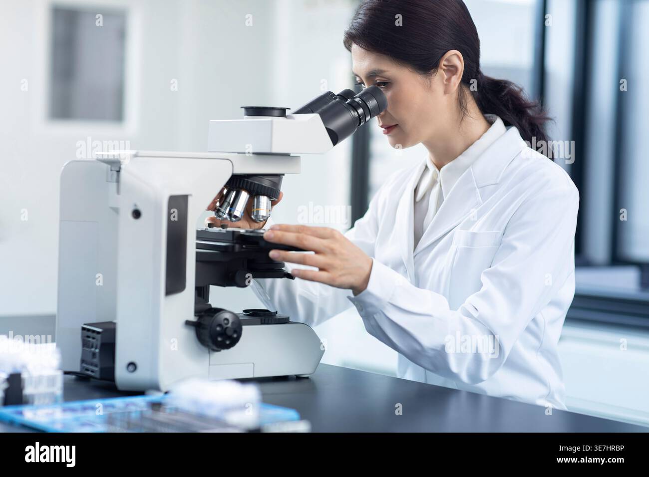 Chinese female scientist looking through microscope while working in laboratory Stock Photo
