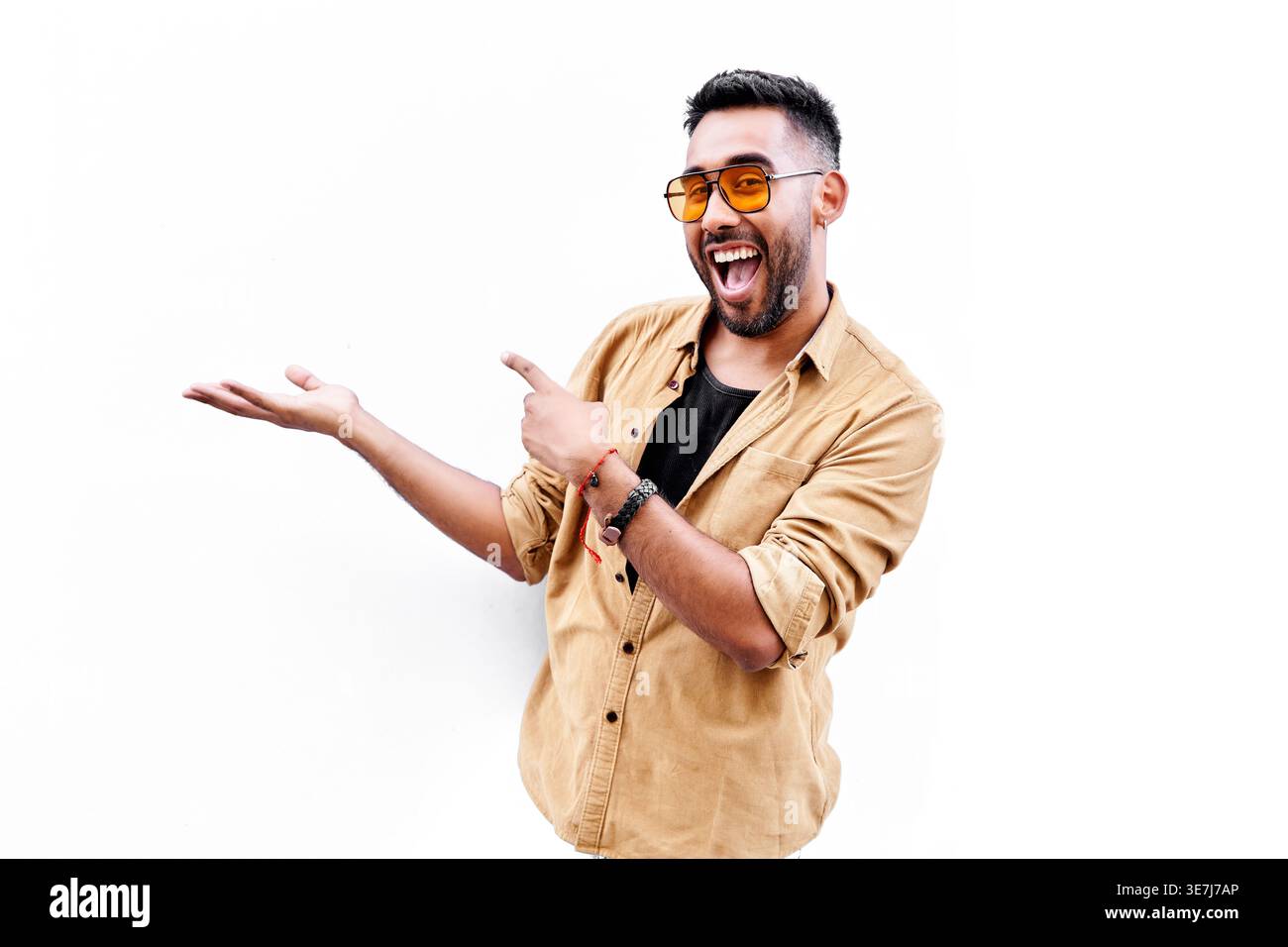 Hispanic man with beard wearing sunglasses pointing sideways showing something while standing against white background in studio Stock Photo