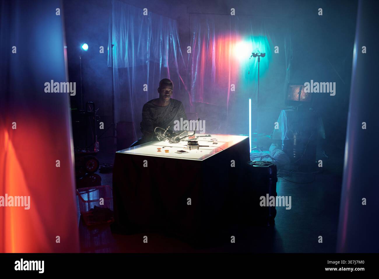 Serious Black man sitting at table with electronic equipment in dark room Stock Photo