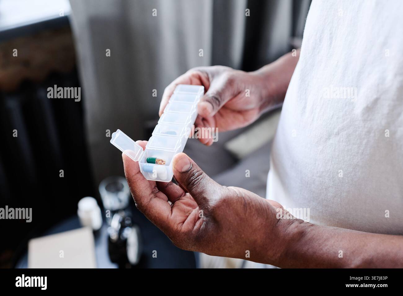 Hands of Black senior man holding plastic container with medicine while standing at home Stock Photo
