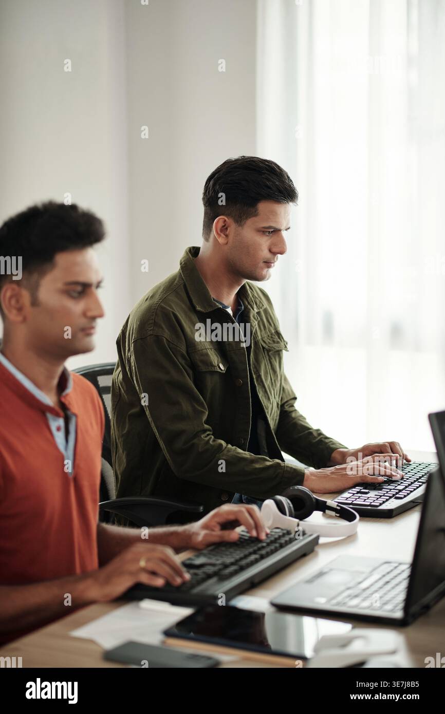 Indian male programmers typing on computer keyboards while sitting at desk in office Stock Photo