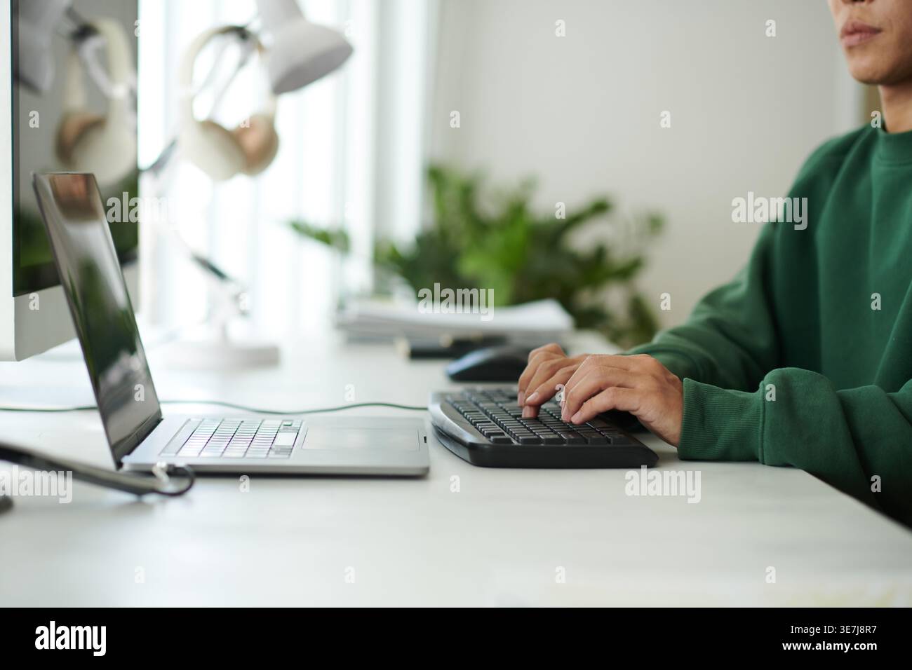 Asian male programmer typing codes on computer while sitting at table with laptop in office Stock Photo
