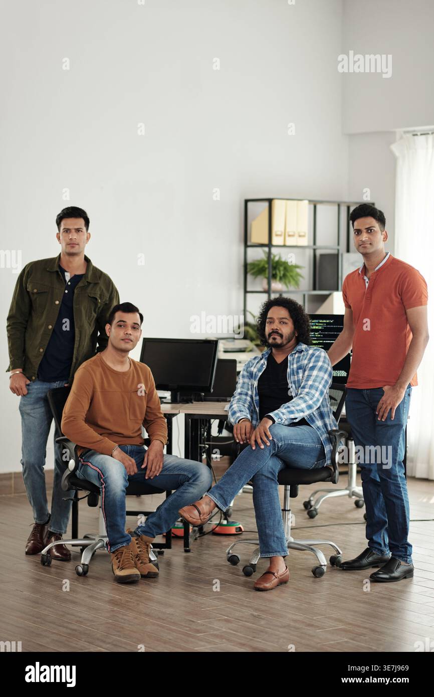 Serious group of Indian businessmen standing and sitting at table with computers in office Stock Photo