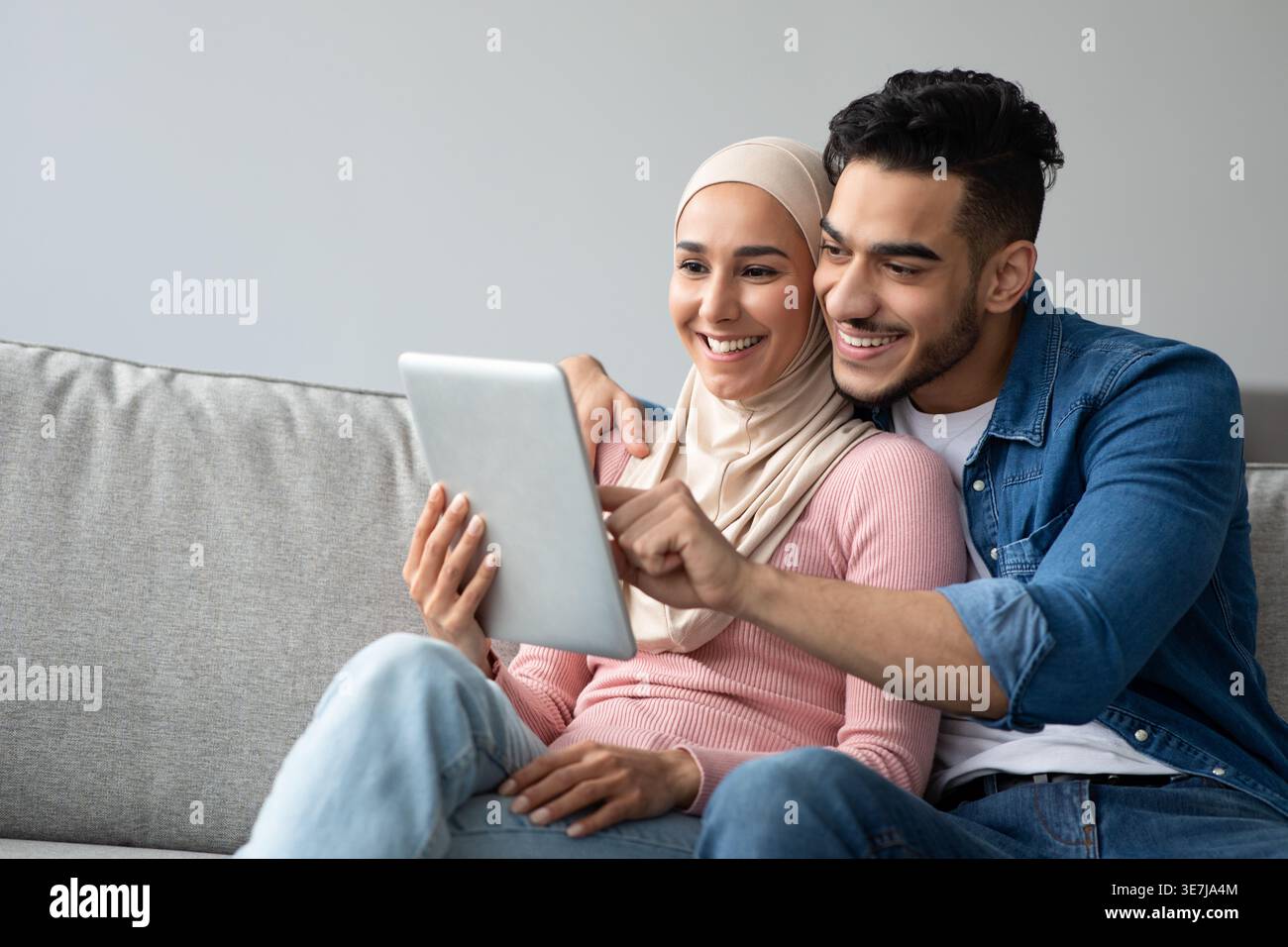 Smiling Middle Eastern couple using tablet while sitting on sofa at home Stock Photo