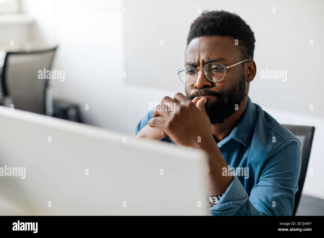 Thoughtful black man in eyeglasses stack with hard task, looking at computer screen, businessman thinking of problem solution, making difficult decisi Stock Photo