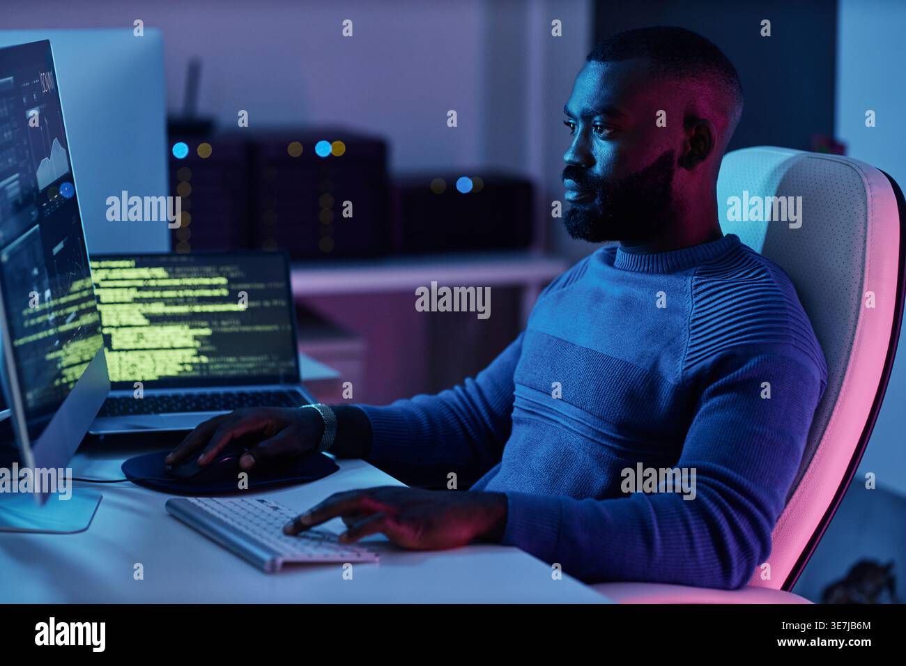 Black male programmer with beard typing codes on computer while sitting at table with laptop in office Stock Photo