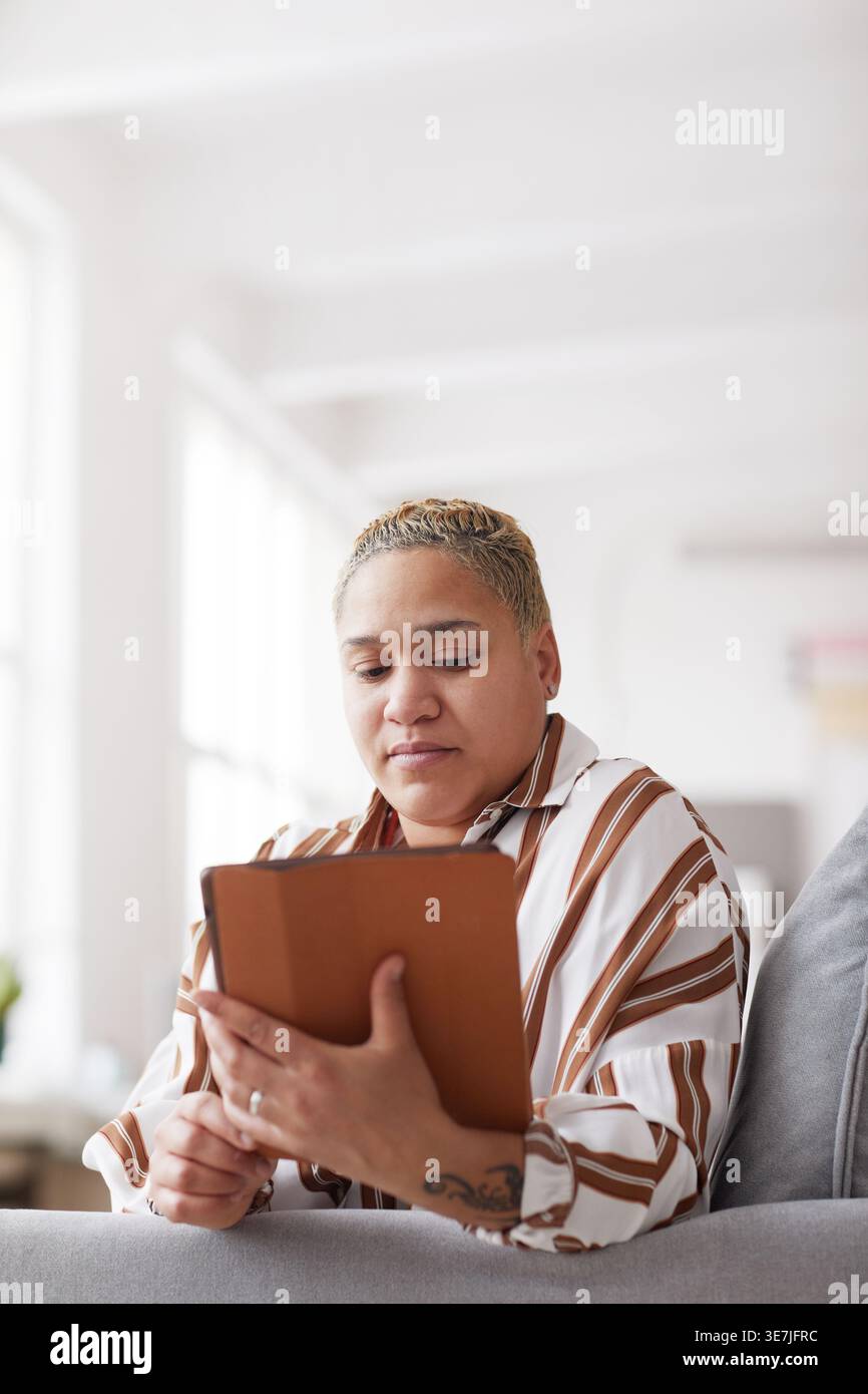 Vertical portrait of modern mixed-race woman holding digital tablet while using online app at home, copy space Stock Photo