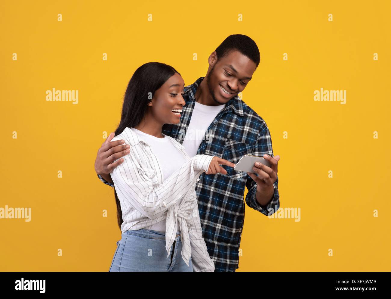 Black couple using smartphone together while standing against yellow background in studio Stock Photo