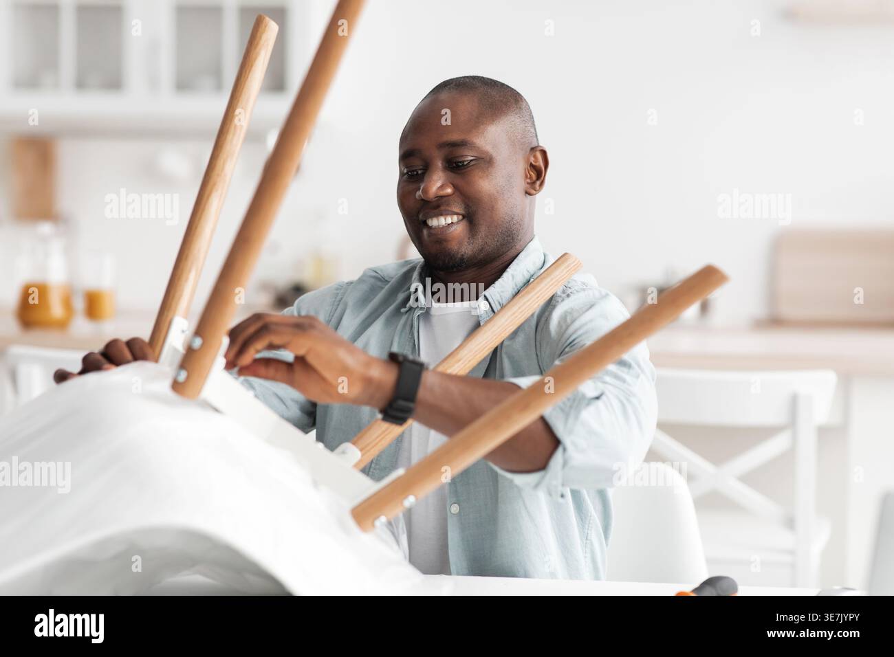 Black man assembling chair standing in kitchen at home Stock Photo