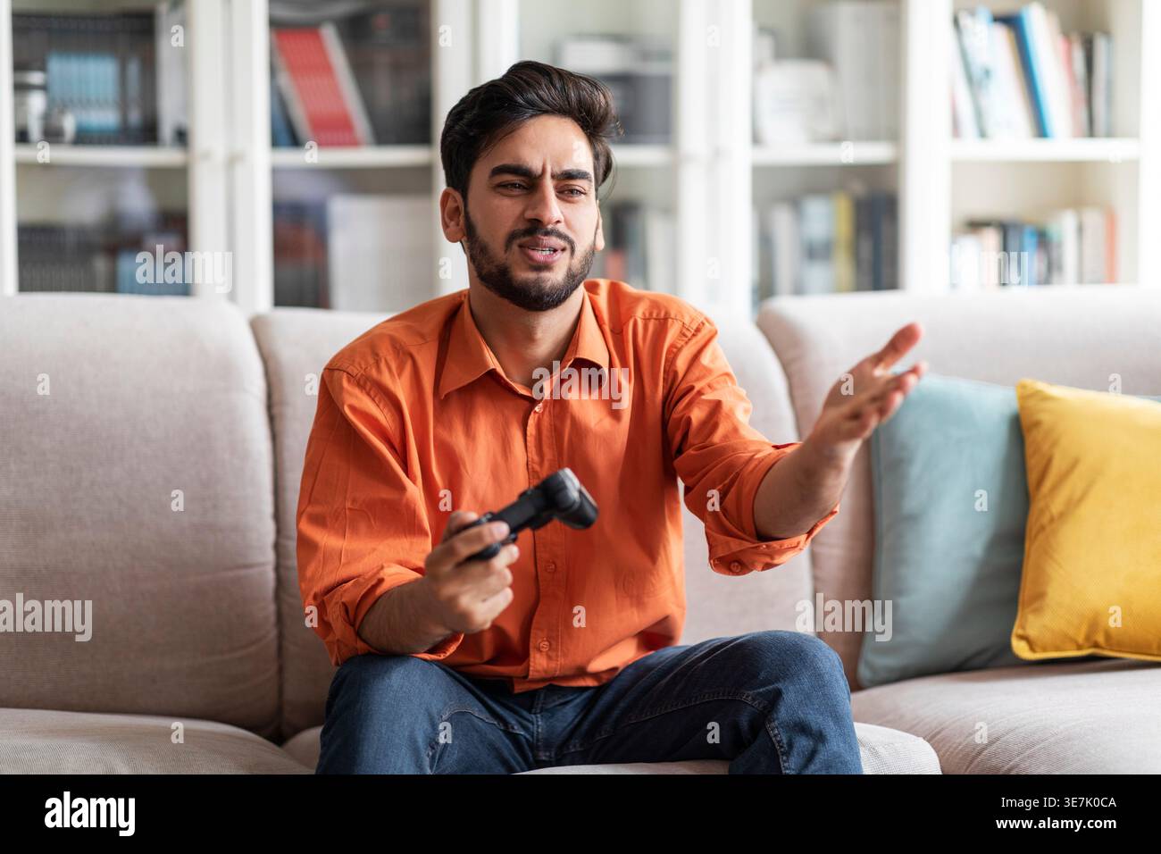 Disappointed Middle Eastern man gesturing hand playing video game sitting on sofa at home Stock Photo