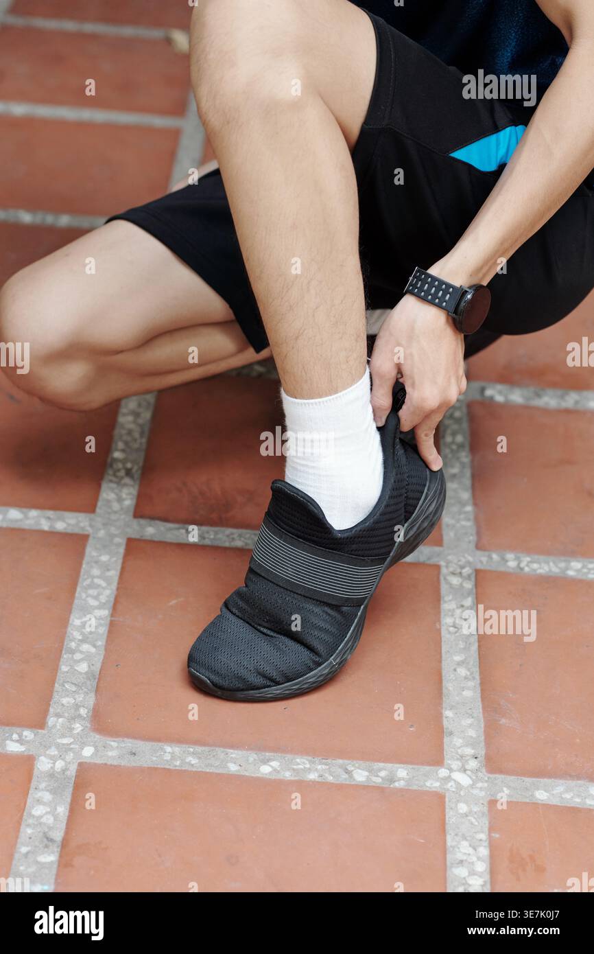 Cropped image of Asian male putting on shoes while crouching on tiles Stock Photo
