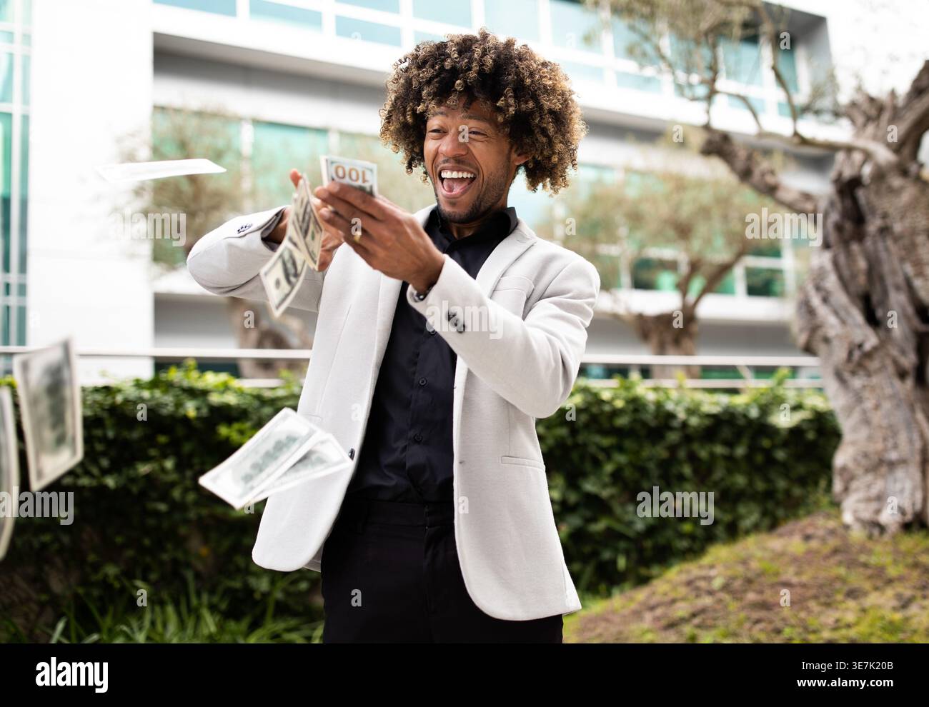 Overjoyed black middle aged businessman throwing money away showing his wealthiness, standing outdoors in park near office building, free space Stock Photo