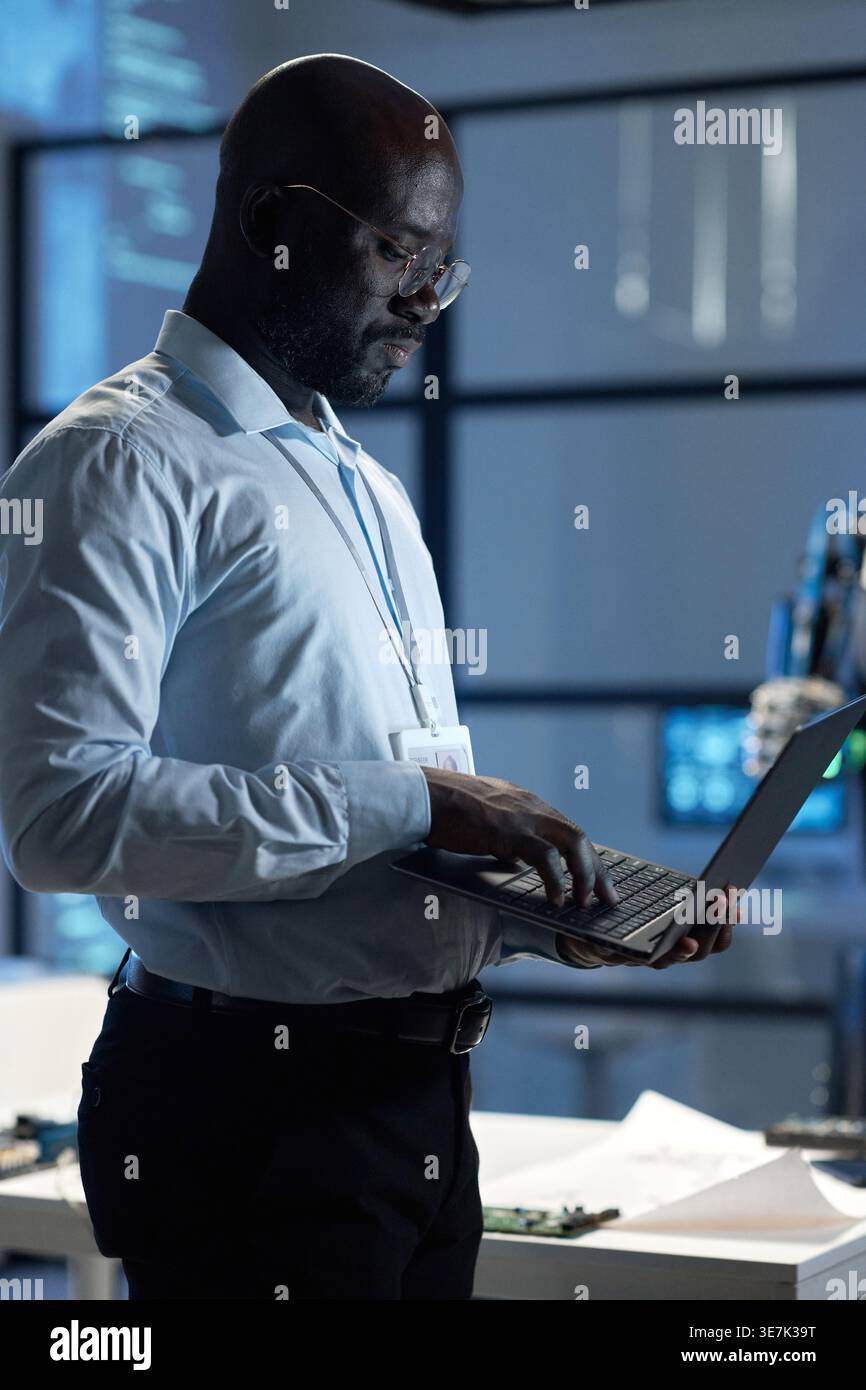 Black male computer engineer with eyeglasses using laptop while standing sideways in laboratory Stock Photo