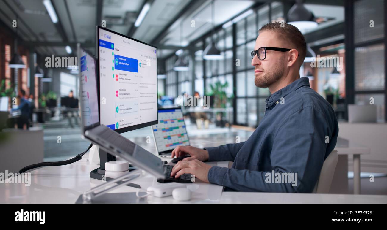 Man Focused On Reviewing Emails On Desktop Computer In A Compact Office Setting Stock Photo