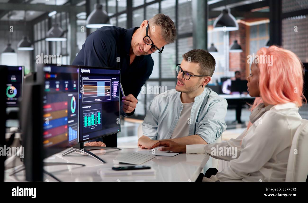 Cybersecurity Engineer Analyzes Data On Screen While Collaborating With Diverse Team. Stock Photo
