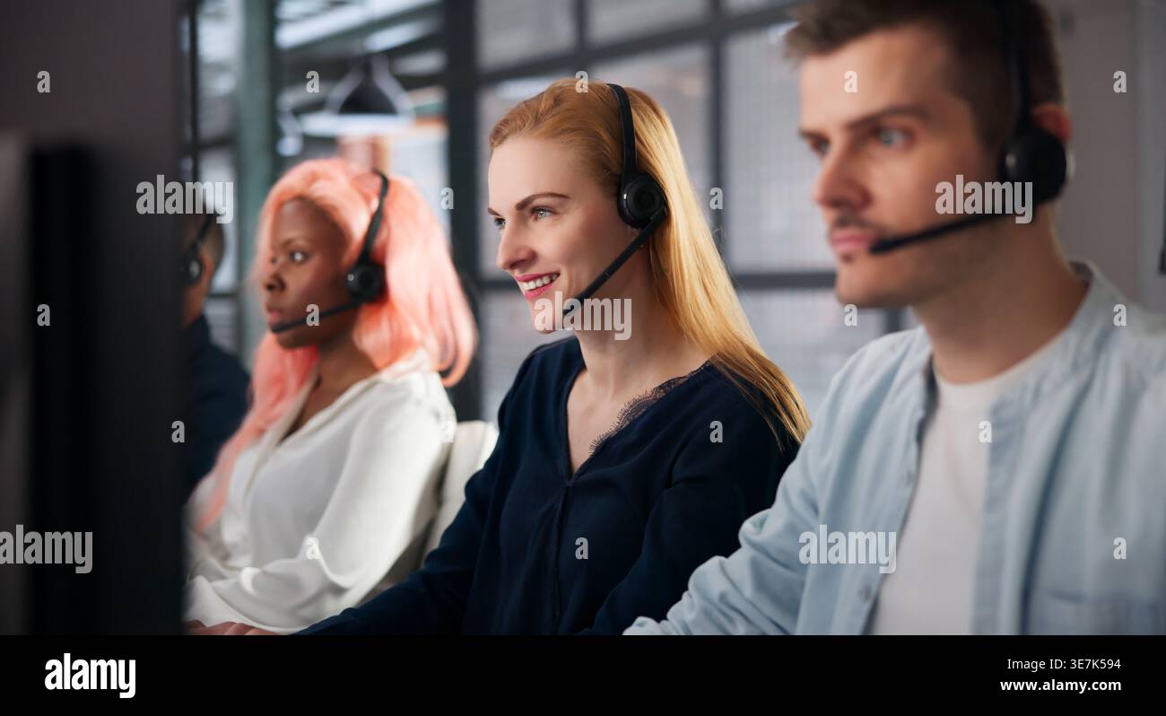 Customer Support Agent Smiles While Talking On Headset At Desk. Stock Photo