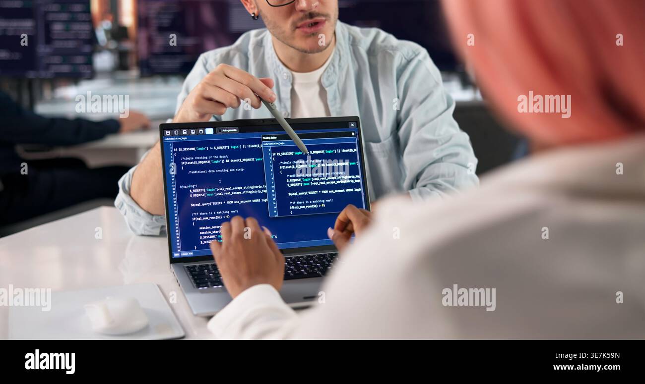 Software Engineer Writes Code On Laptop While Discussing Project With Team. Stock Photo