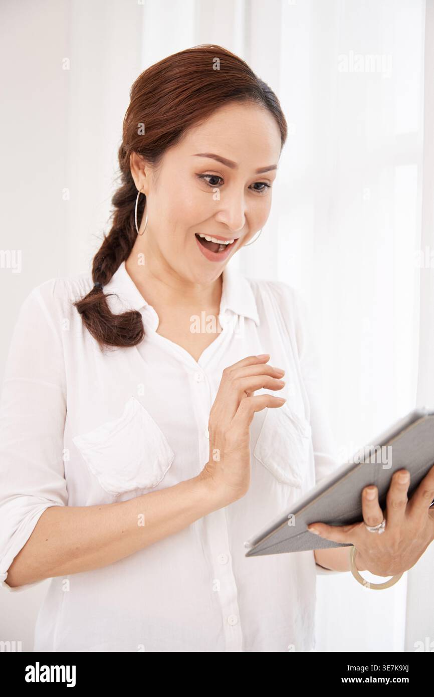 Surprised Asian woman using tablet while standing at home Stock Photo