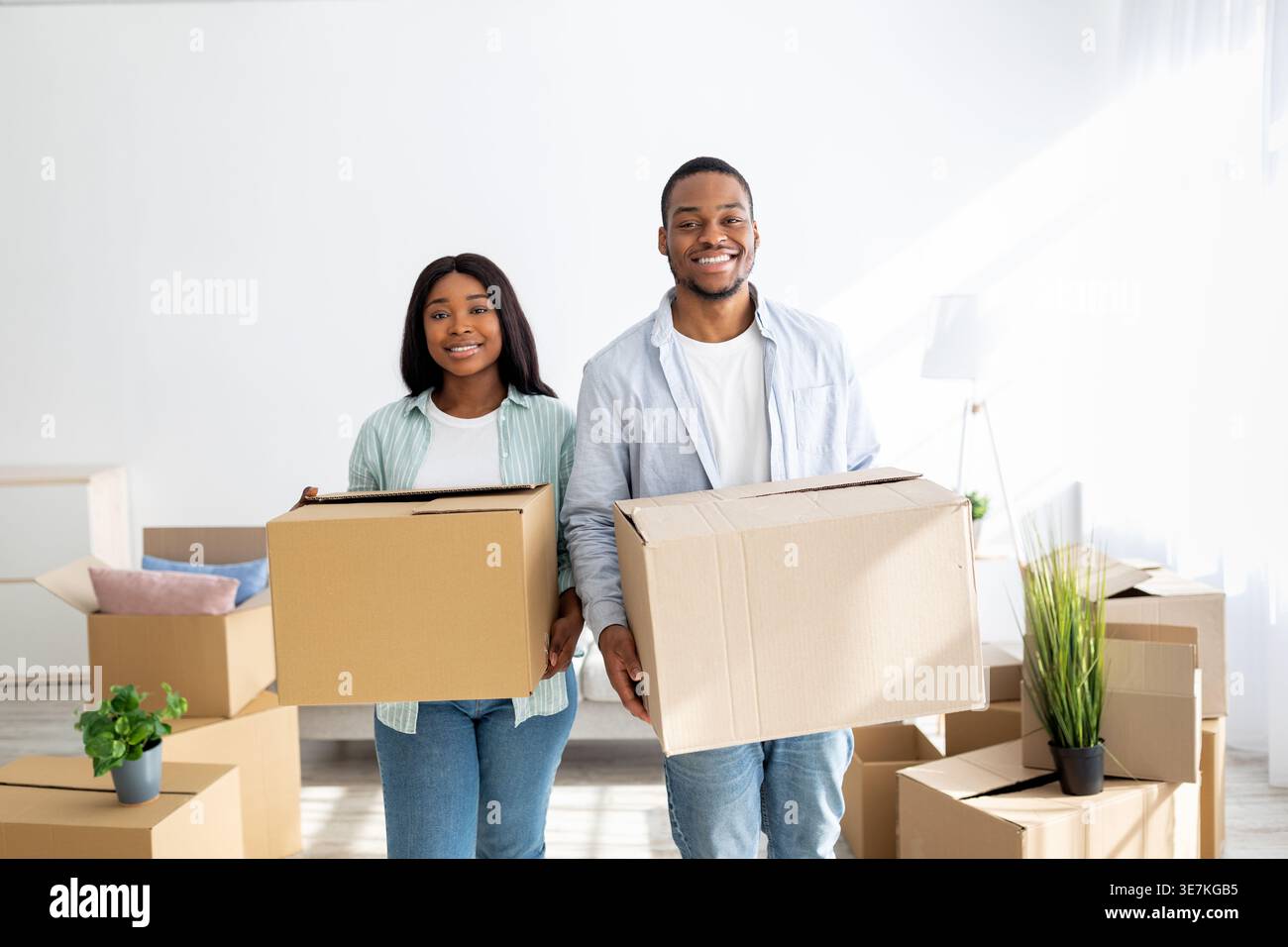 Smiling Black couple holding cardboard boxes standing in living room at home Stock Photo