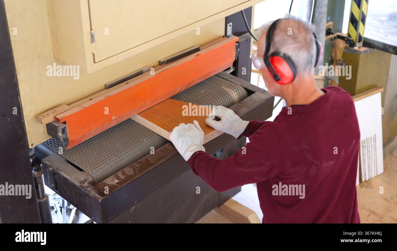 Carpenter sanding wood plank using belt sander machine Stock Photo