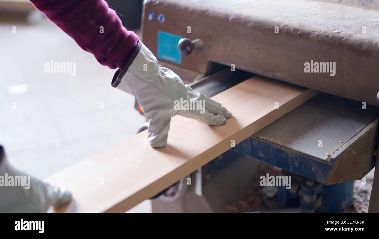 Worker planing wood plank using thickness planer in workshop Stock Photo