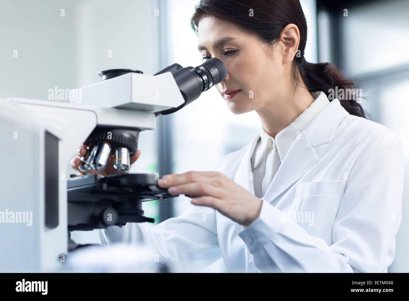 Chinese female scientist looking through microscope while working in laboratory Stock Photo