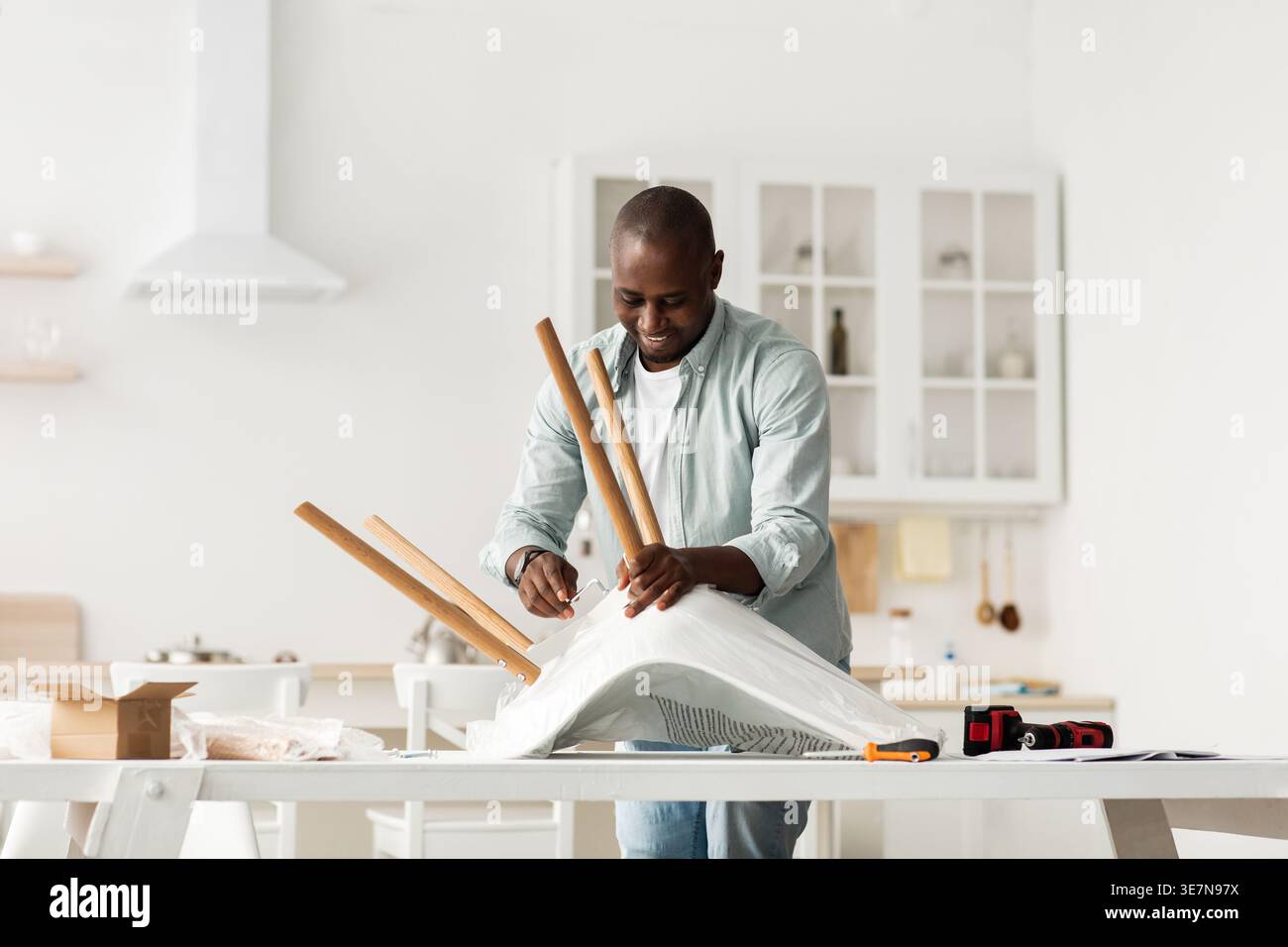 Black man assembling chair standing in kitchen at home Stock Photo