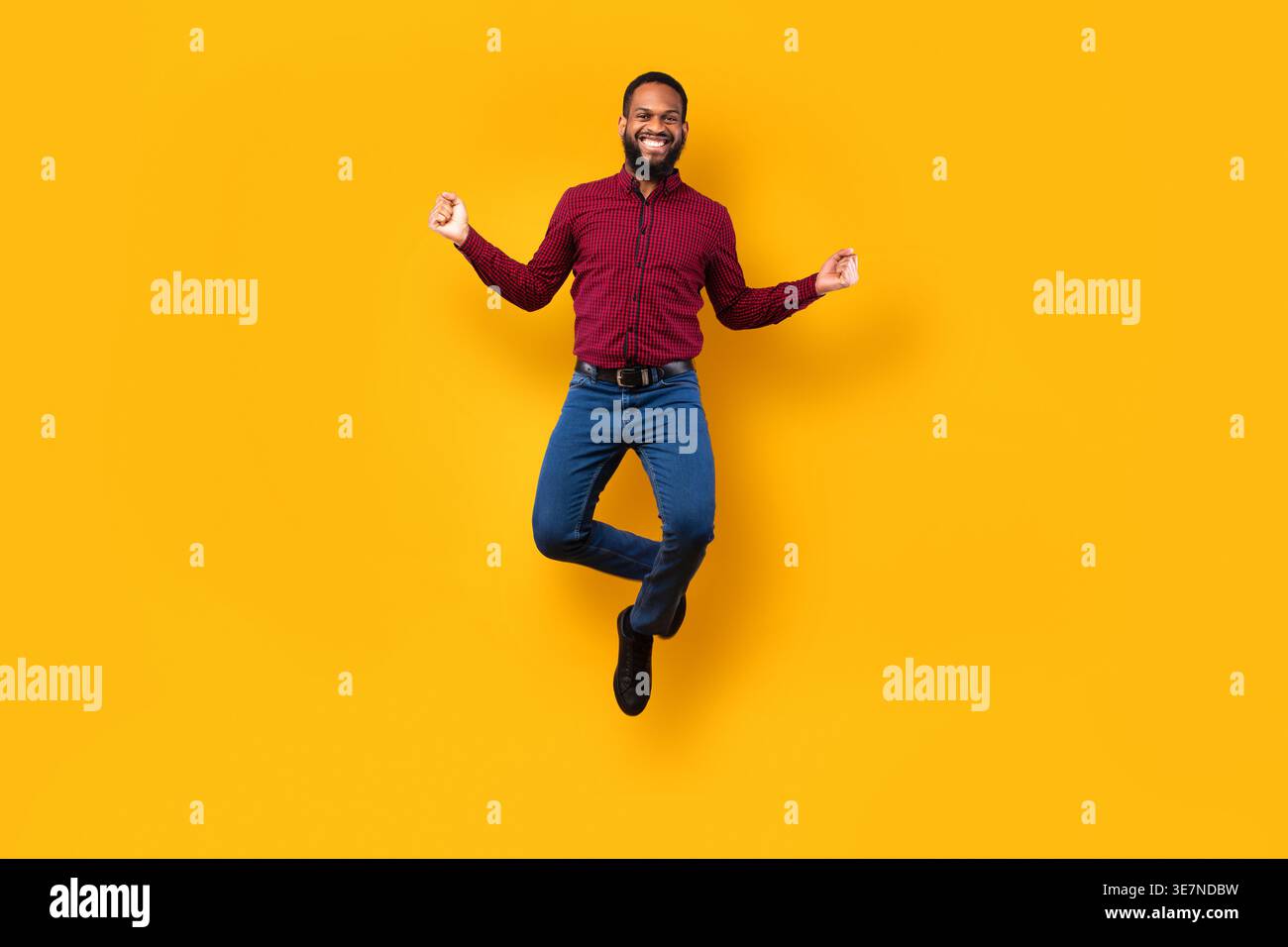 Black man jumping against yellow background in studio Stock Photo