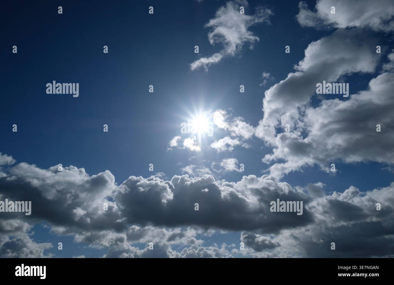 backlit sunburst behind clouds on blue sky background Stock Photo