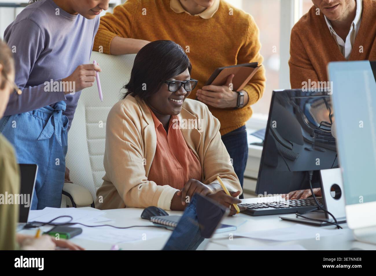 Diverse group of programmers working together on computer sitting and standing in office Stock Photo