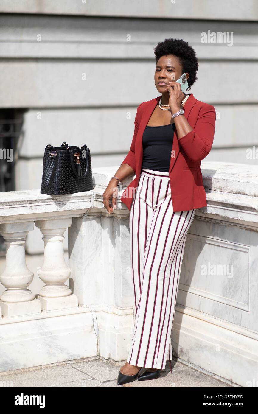 A well-dressed woman in a red blazer and striped pants stands by a white  stone balustrade, talking on a smartphone. She exudes confidence and  professi Stock Photo - Alamy