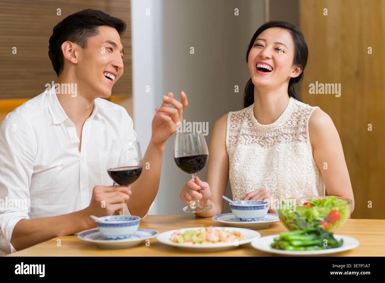 Cheerful Chinese couple holding glass of wine having a dinner while sitting at table at home Stock Photo