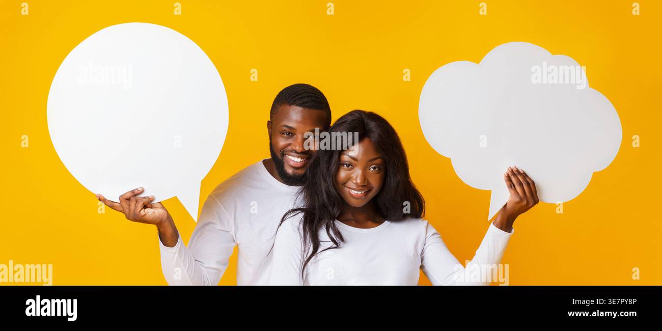 Black couple holding empty speech bubbles while standing against yellow background Stock Photo