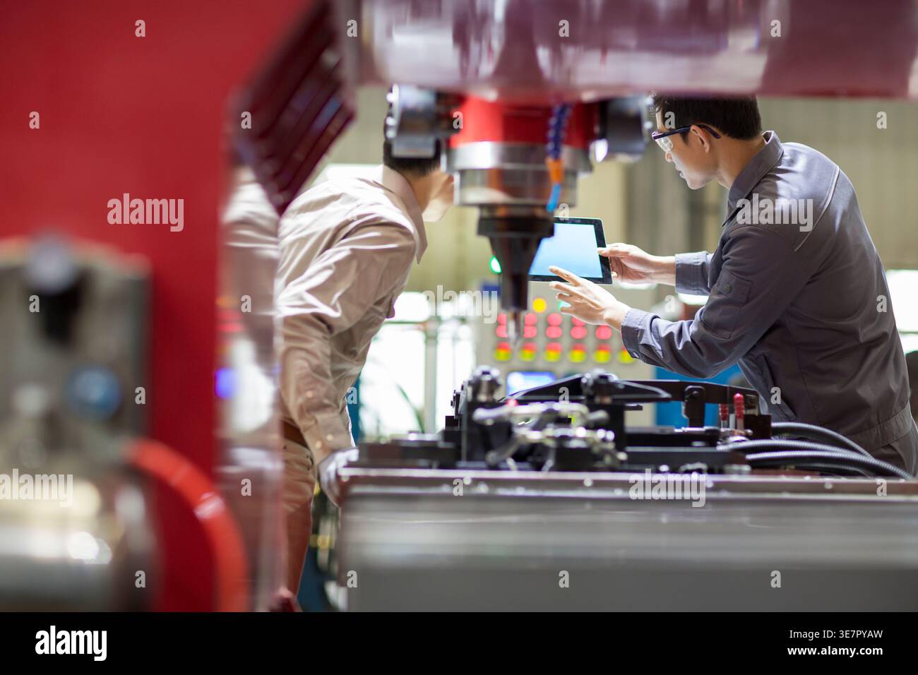 Chinese male engineers checking machine using tablet standing in factory Stock Photo