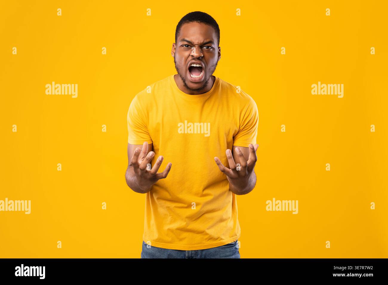 Black man shouting with opened hands while standing against yellow background in studio Stock Photo
