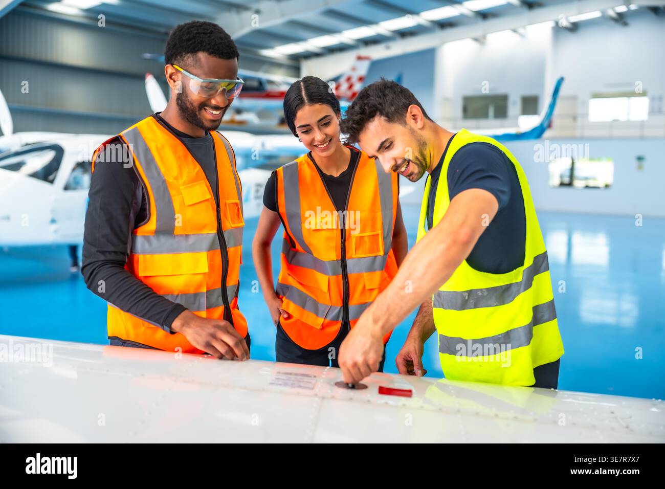 Diverse aircraft maintenance crews inspecting airplane wing in hangar Stock Photo
