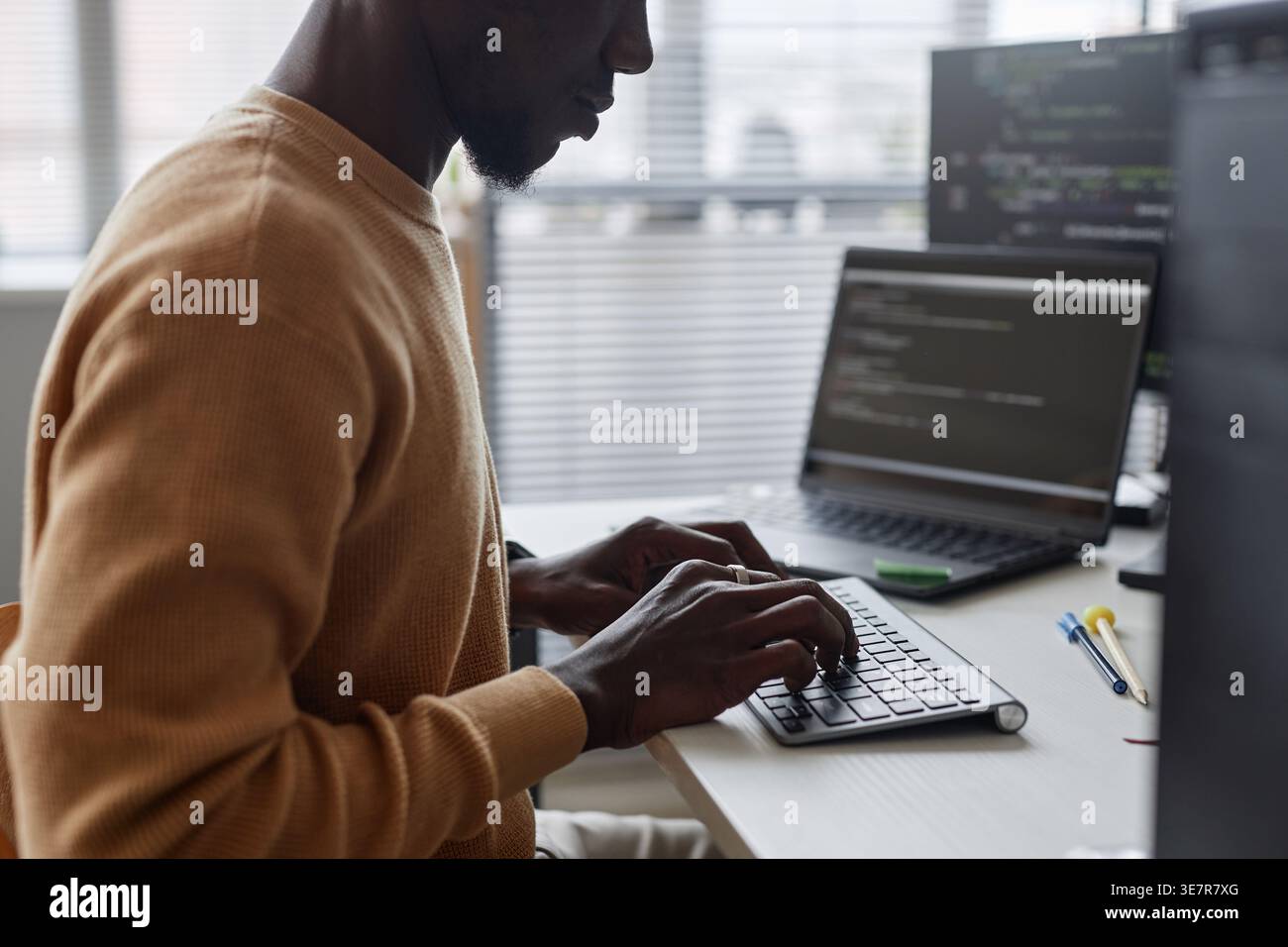 Black male programmer typing codes on computer sitting at table with laptop in office Stock Photo