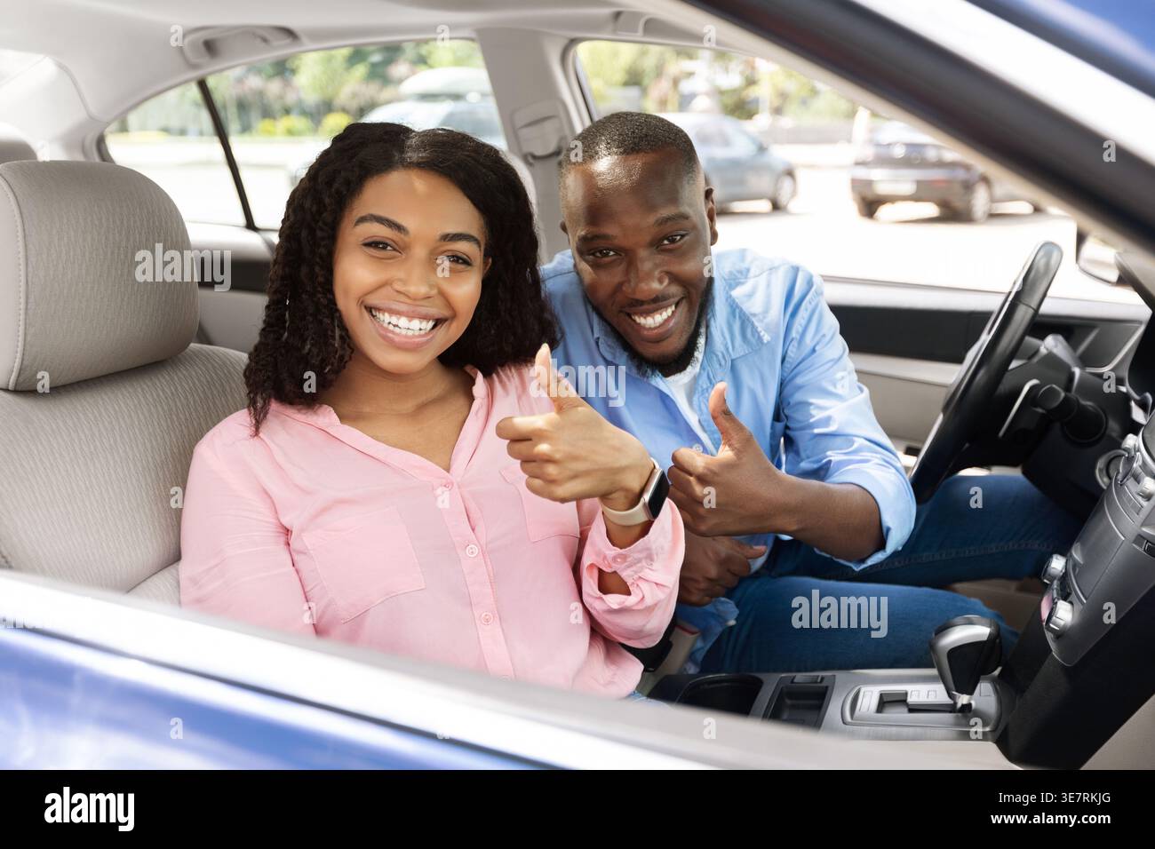 Smiling Black couple gesturing thumbs up while riding car together in city Stock Photo