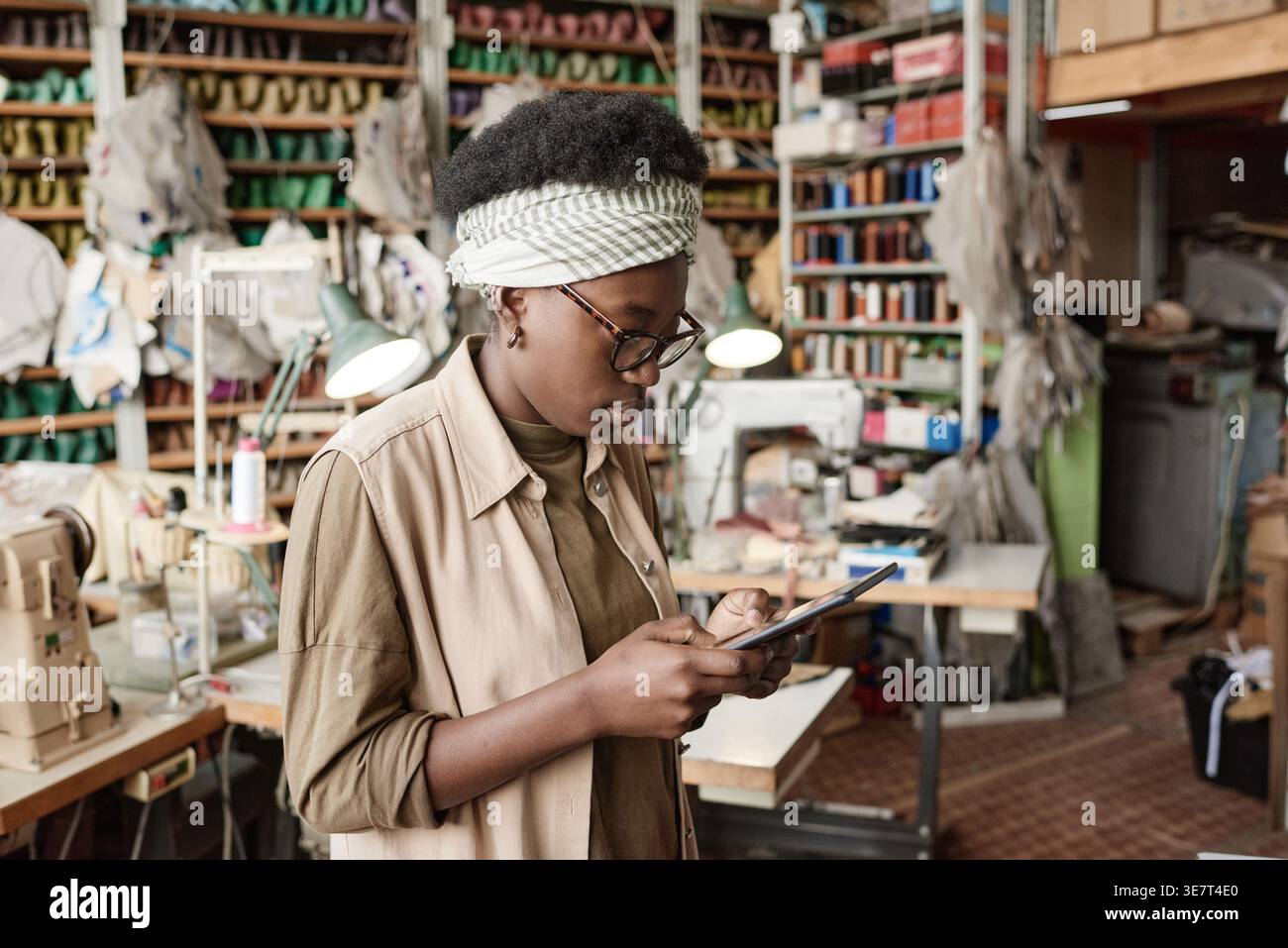 Black female designer wearing eyeglasses using tablet while standing in workshop Stock Photo