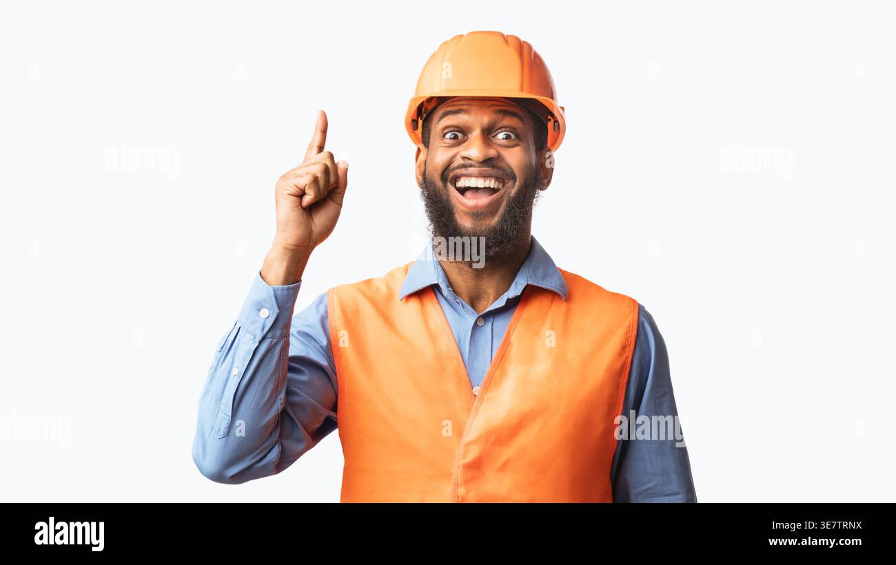 Black male worker wearing safety helmet pointing finger up while standing against white background in studio Stock Photo