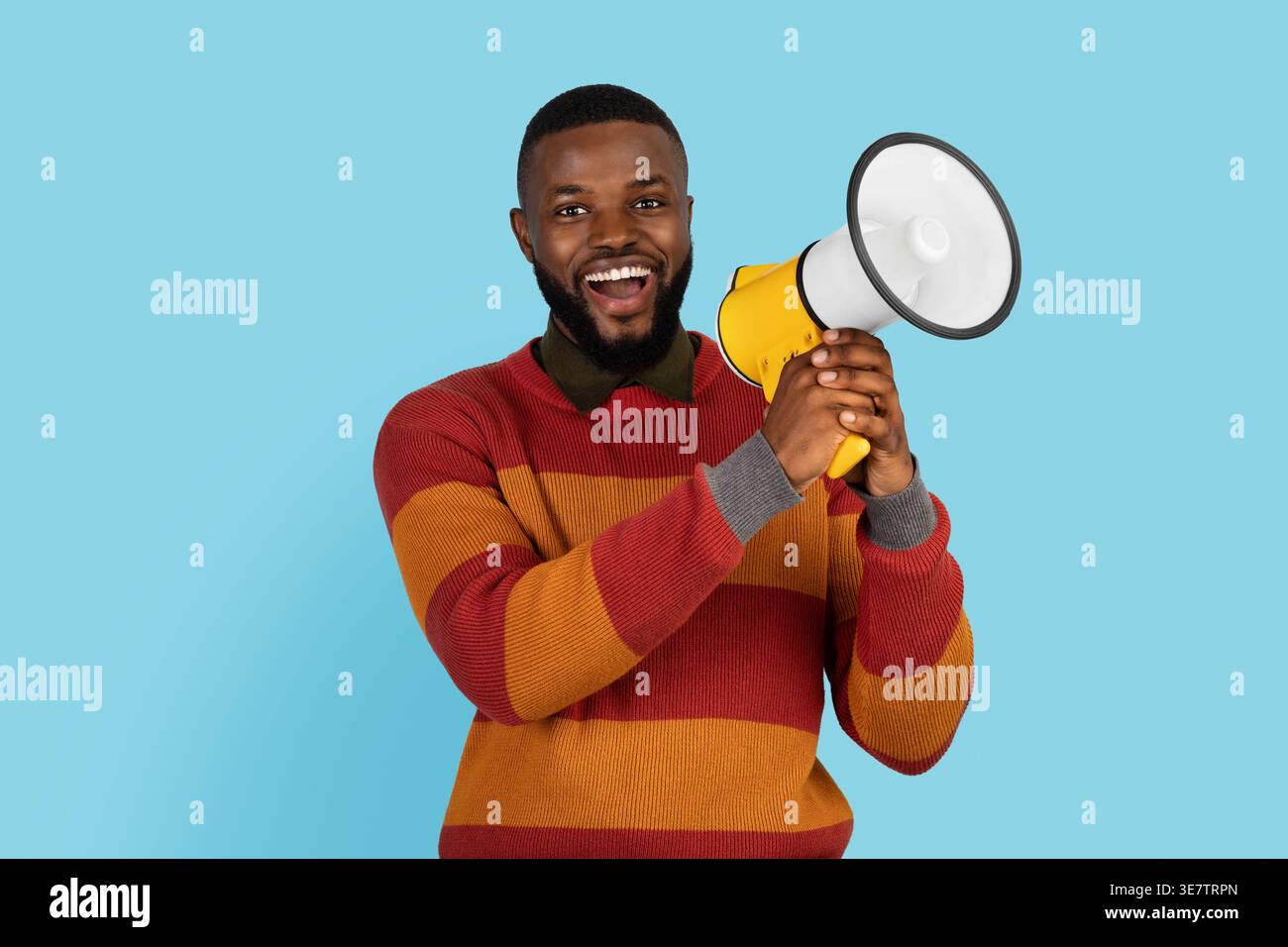 Smiling Black man holding megaphone while standing against blue background in studio Stock Photo