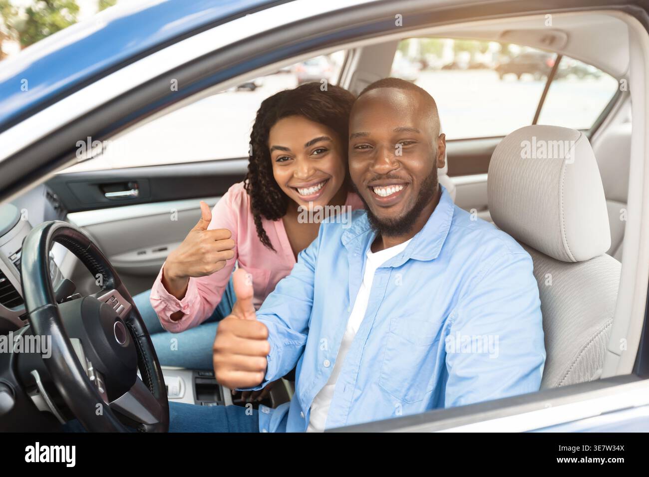 Smiling Black couple gesturing thumbs up while riding car together in city Stock Photo