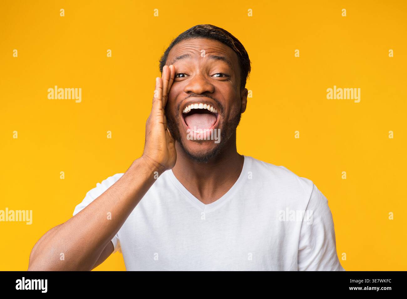 Hey. Positive African American Man Shouting Holding Hand Near Mouth Standing On Yellow Studio Background Stock Photo