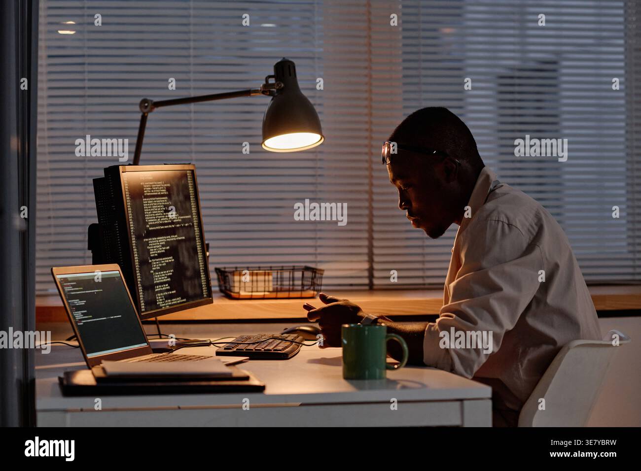 Focused Black male programmer in eyeglasses examining computer codes working overtime in office Stock Photo