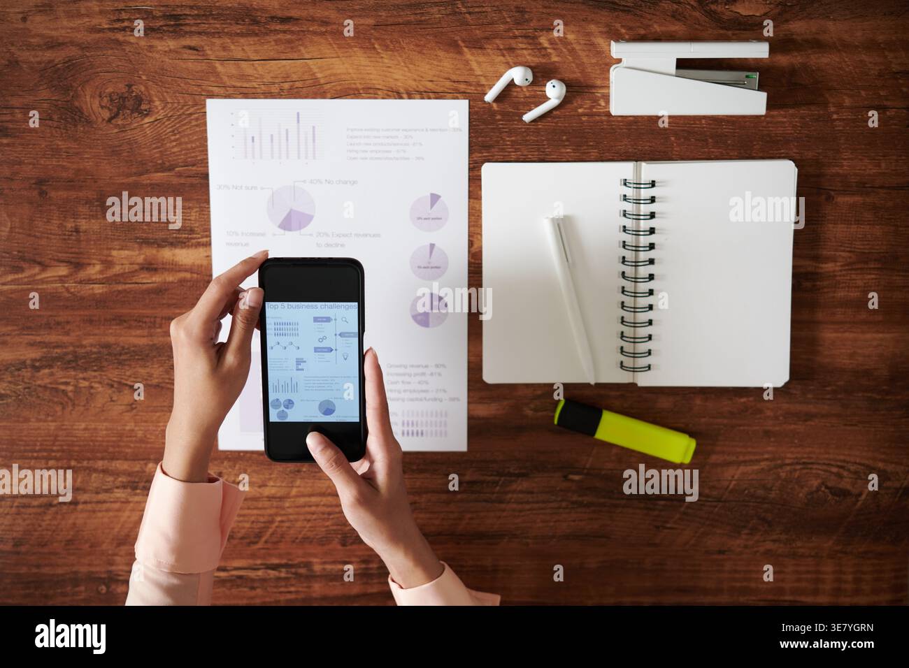 Female designer using smartphone while sitting at table with notebook and documents in office Stock Photo