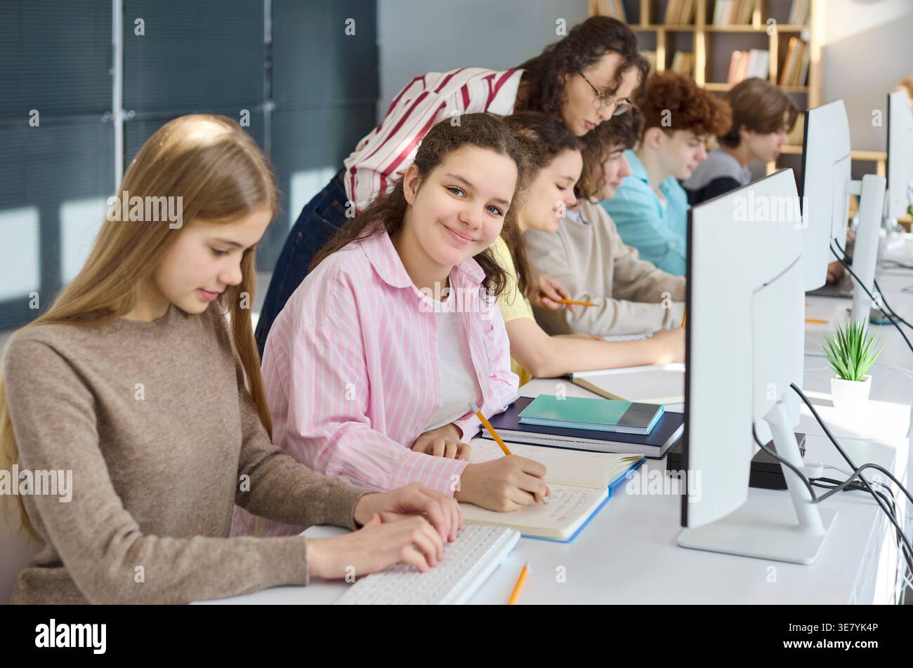 High school students coding at computers with teacher help in modern classroom Stock Photo