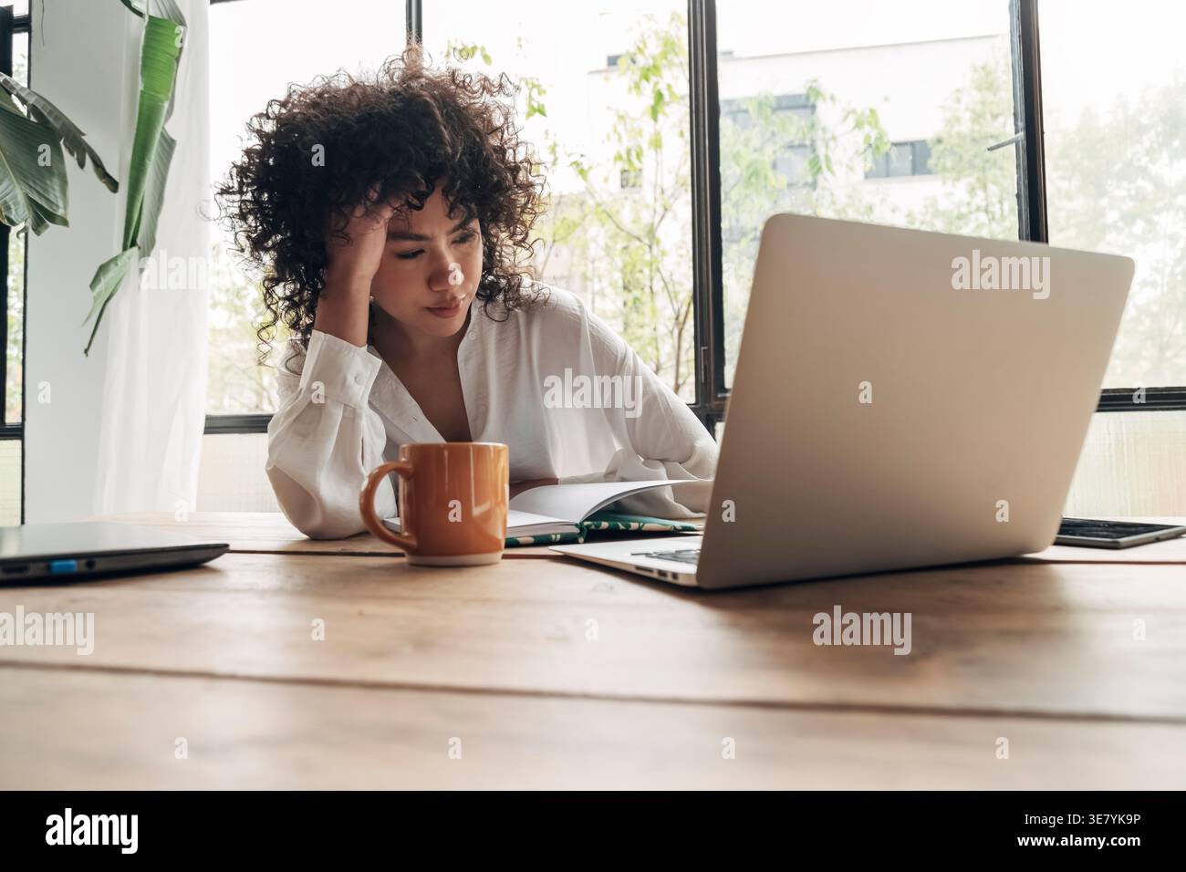 Hispanic woman sitting at table touching forehead during work at home Stock Photo