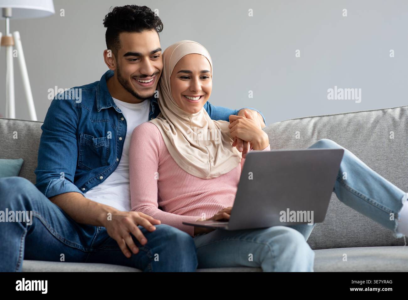 Smiling Middle Eastern couple using laptop while sitting close together on sofa at home Stock Photo