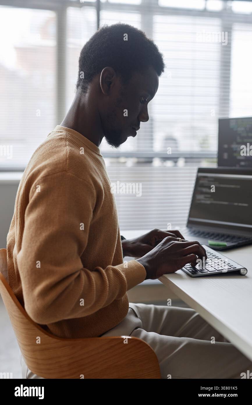 Black male programmer typing codes on computer sitting at table with laptop in office Stock Photo