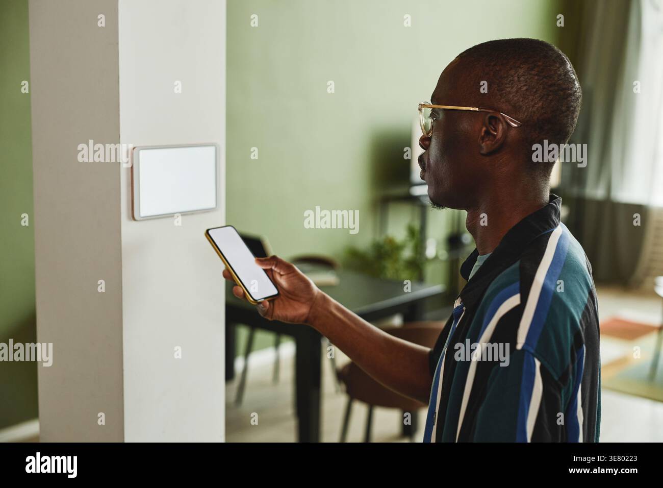 Black man using smartphone while connecting to smart home system standing indoors Stock Photo